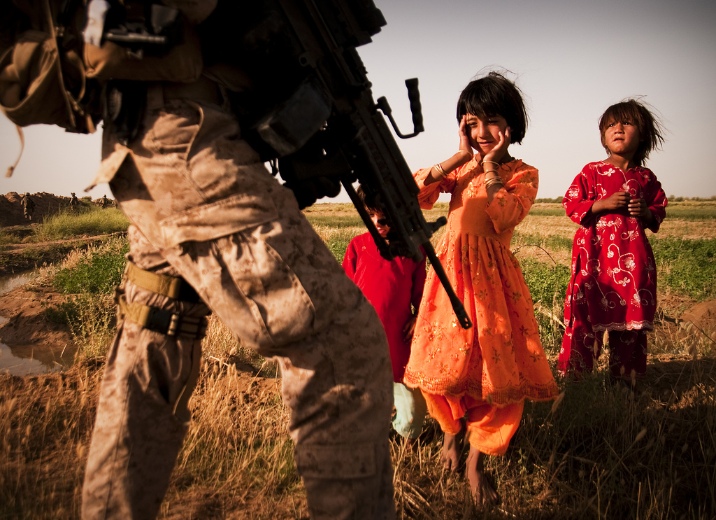 HELMAND PROVINCE, Afghanistan — Afghan girls watch as Lance Cpl. Karl Schmidt, squad automatic weapon gunner, guard force, Headquarters and Service Company, 3rd Battalion, 3rd Marine Regiment, makes his way to set up a vehicle checkpoint May 30, 2010