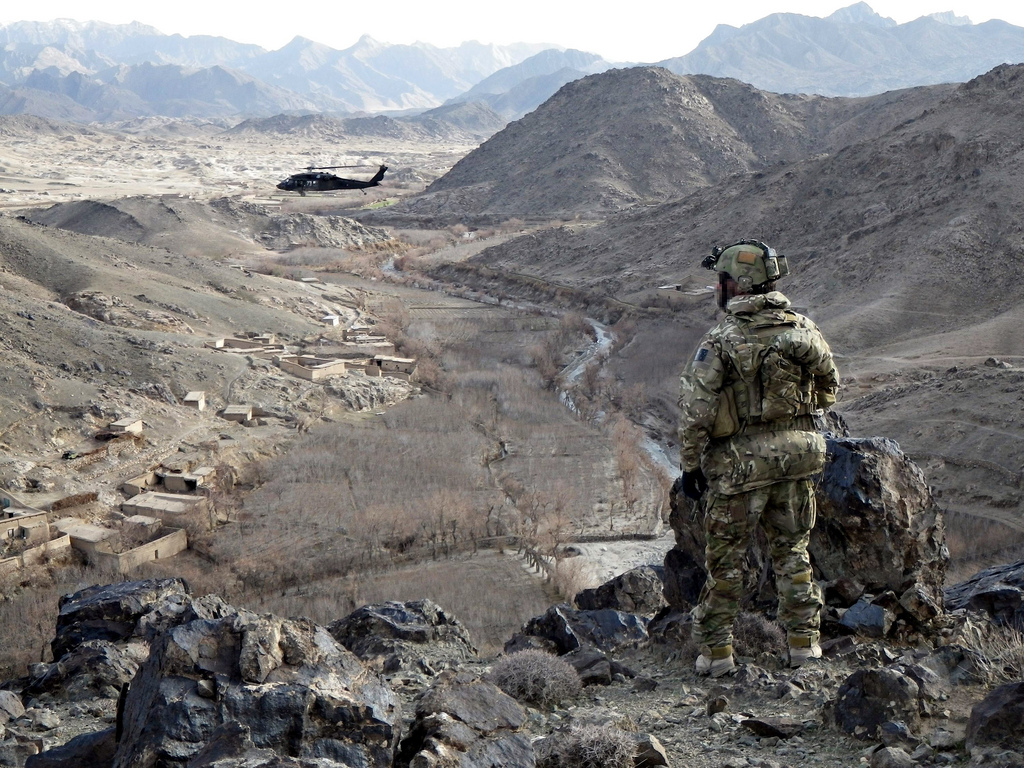 A Special Forces soldier observes a valley in Uruzgan as a Blackhawk circles above.