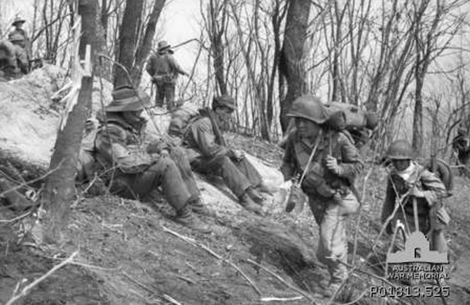 Hill Salmon, Korea, 1951-04-17. Carrying heavy loads on their backs, soldiers (right) of K Company, 19th Regimental Combat Team (RCT), 6th Republic of Korea (ROK) Infantry Division, arrive on Hill Salmon to relieve C Company, 3rd Battalion, The Royal Australian Regiment (3RAR). Two Australian soldiers (left) are sitting on the ground with their packs on their backs, ready to move out. The ROKs abandoned the hill to Chinese forces when they attacked a few days later. (Donor I. Robertson)