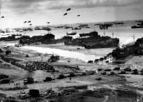 Landing ships putting cargo ashore on one of the invasion beaches, at low tide during the first days of the Normandy invasion, June 1944. Among identifiable ships present are USS LST 532 (in the centre of the view); USS LST 262 (third LST from right); USS LST 310 (second LST from right); USS LST 533 (partially visible at far right); and USS LST 524. Note the barrage balloons overhead and the Army "half-track" convoy forming up on the beach.