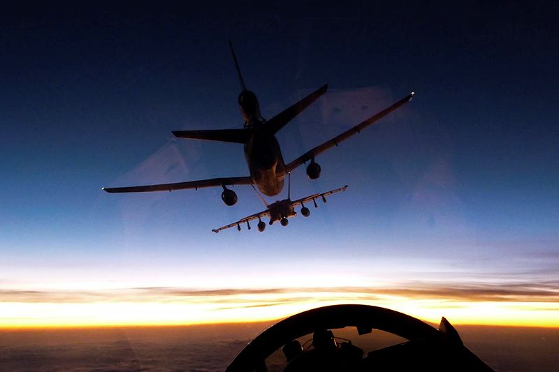 The wingman of a Royal Australian Air Force (RAAF) F/A-18F Super Hornet watches as his leader prepares to refuel from a United States Air Force KC-10A tanker aircraft mid-air as the sun sets over Iraq.
