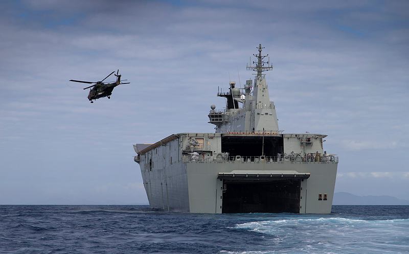 A MRH 90 helicopter takes off from HMAS Canberra's flight deck while the ship is docked down and conducting landing craft operations.